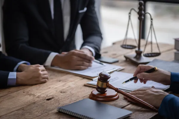 Blick auf einen Schreibtisch, auf dem Verträge liegen, im Hintergrund Justizias Waage